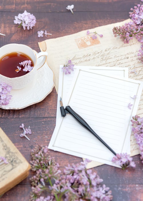 ティーカップに浮かぶ花弁と白紙の手紙の写真