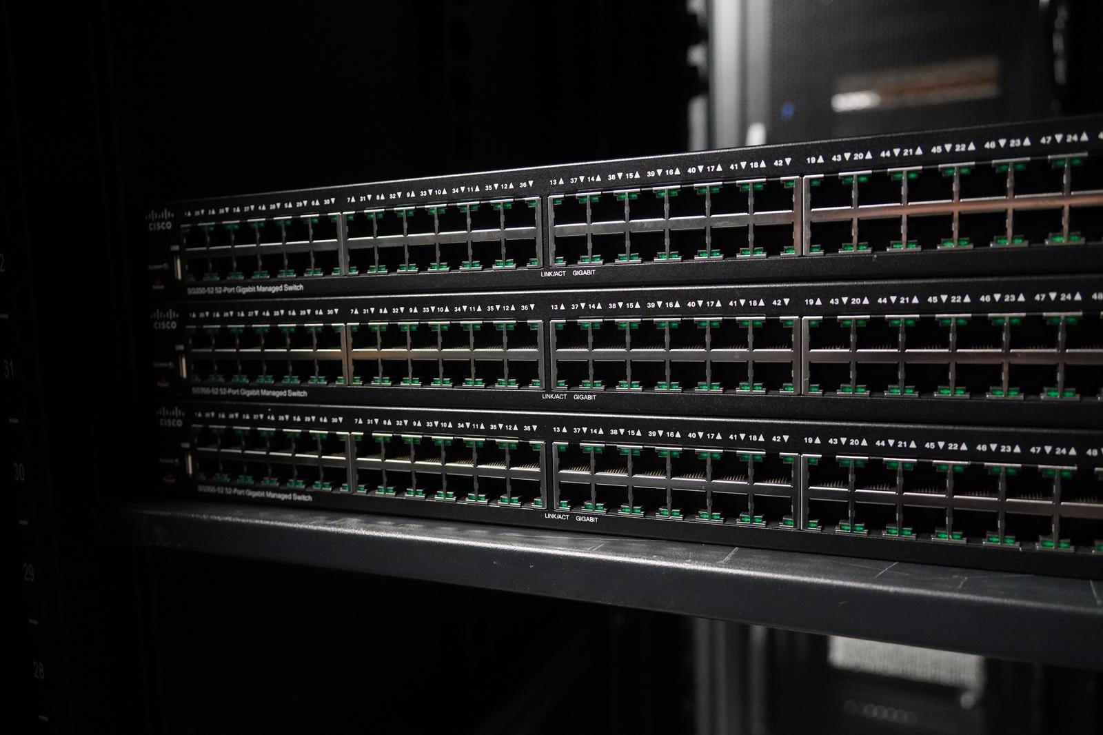 暗いラック内にマウントされた複数段のCiscoネットワークスイッチ、グリーンのLED点灯