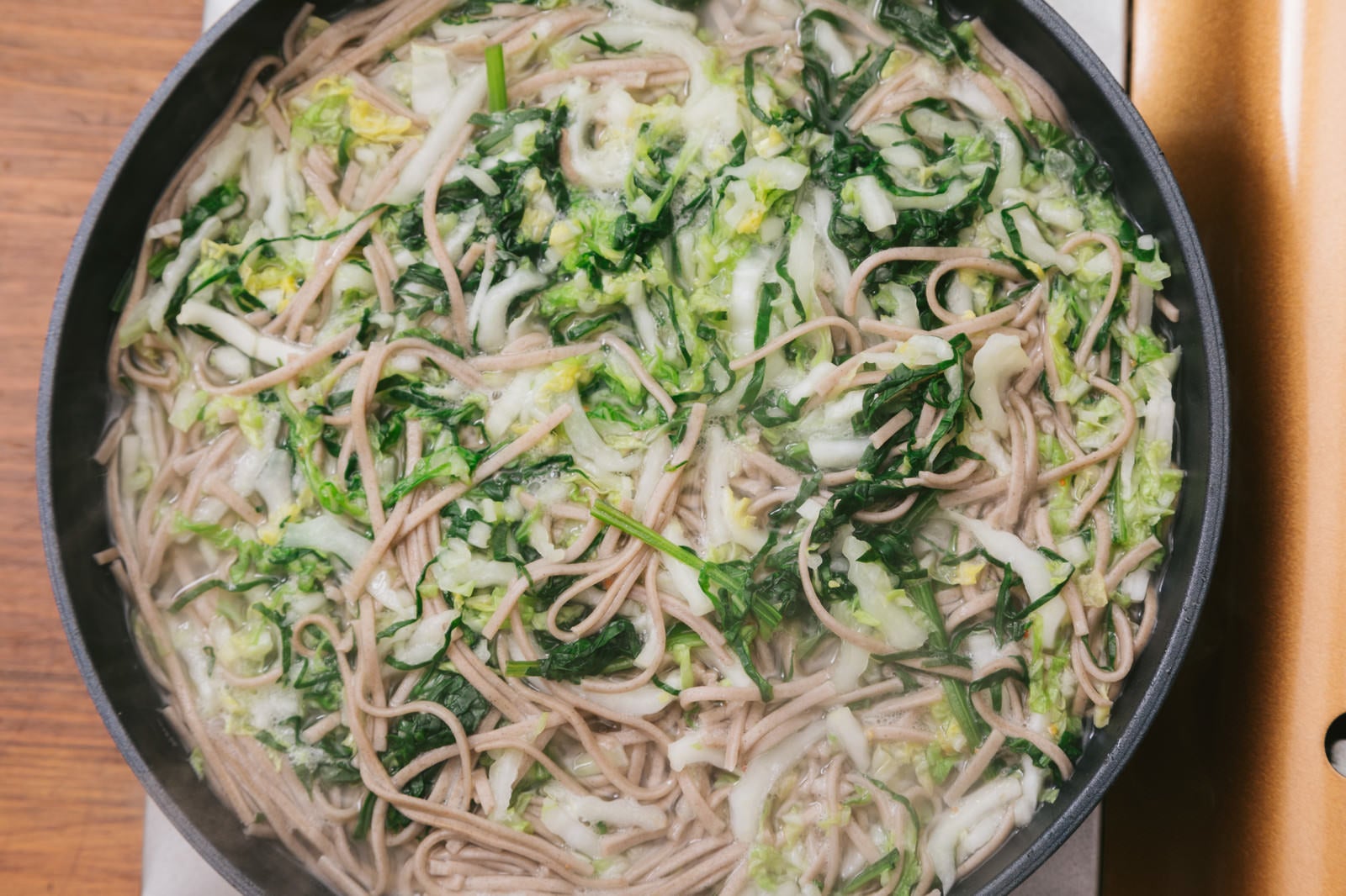 「鍋にお湯を沸かしてそばと大根、白菜、ほうれん草を加える」の写真