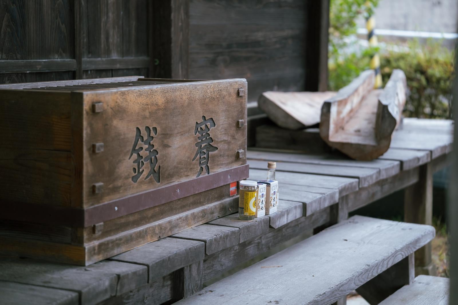 「岳温泉の賽銭箱前に置かれた酒」の写真