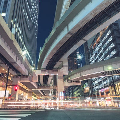 池袋のビル群と首都高下の光跡、夜間の横断歩道と車の光の流れの写真