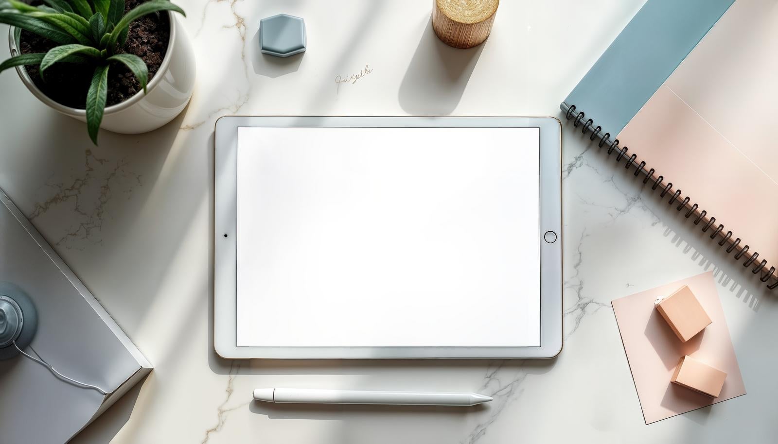 マーブルのテーブルにタブレットやペン、観葉植物、ノートがフラットレイで並んでいる