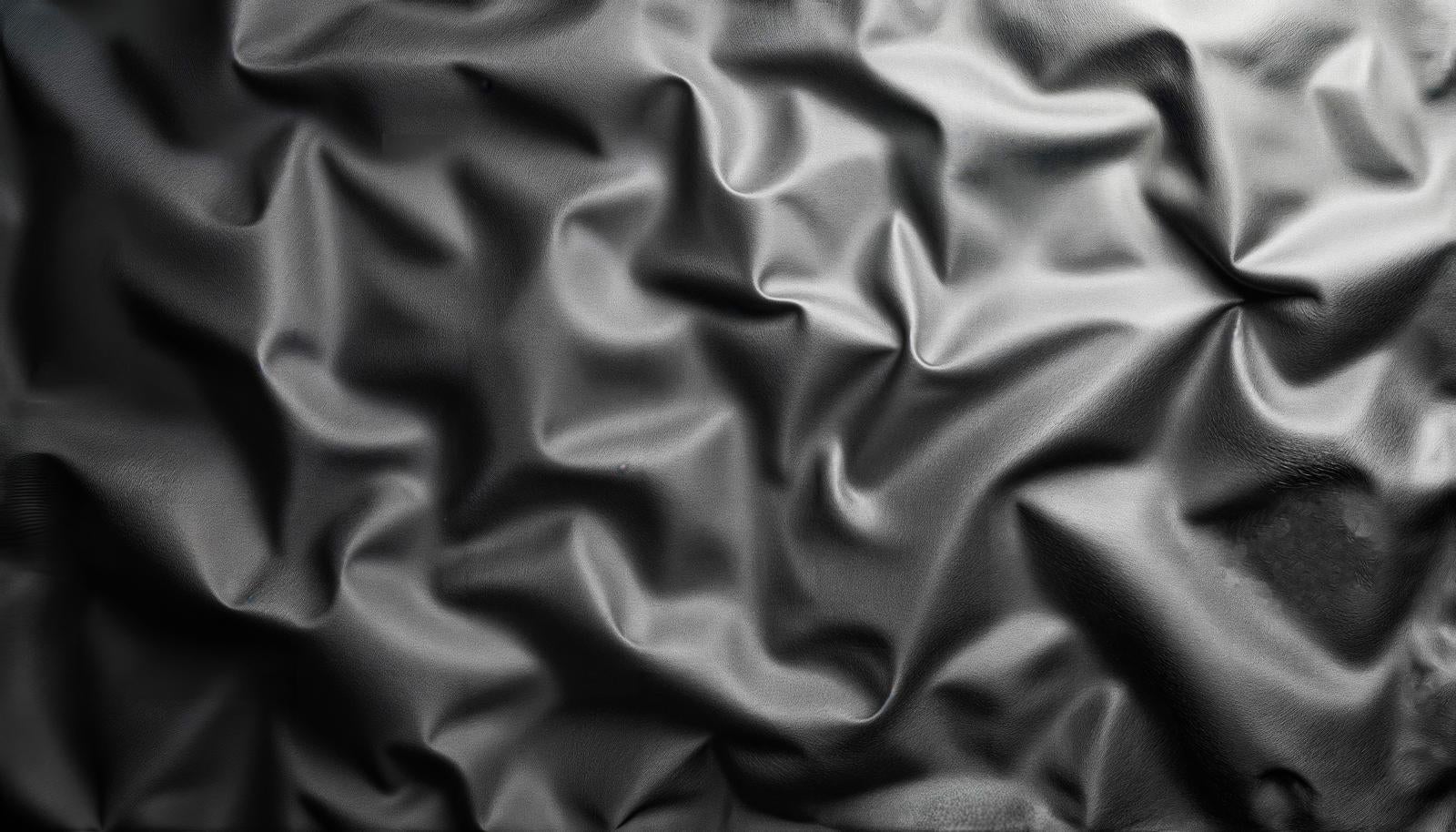 Texture of crumpled black vinyl material surface with light highlighting wrinkles and creases creating polygon-like surfaces