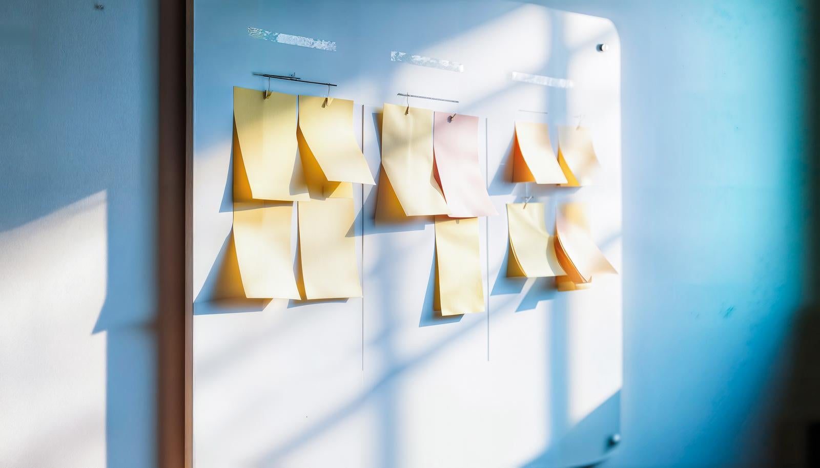窓からの光が差し込むホワイトボードに複数の付箋メモがクリップで留められている