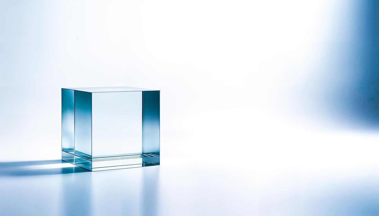 白い背景の上に透明なアクリルキューブが1つ置かれ、淡い青い光を帯びている
