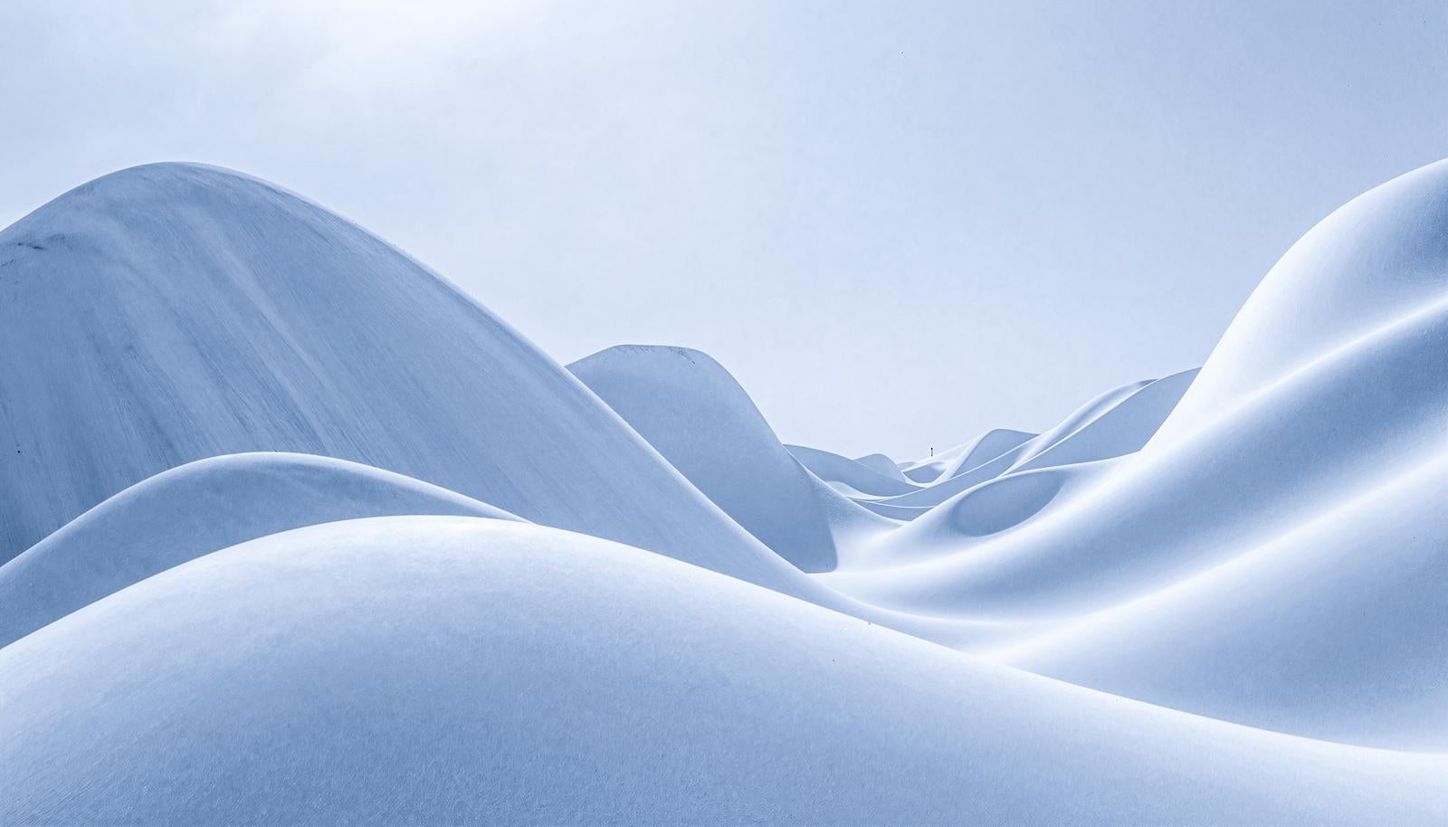 Multiple wave-shaped snowy hills stretching across the landscape, appearing three-dimensional through the interplay of light and shadow in this winter snowy scene