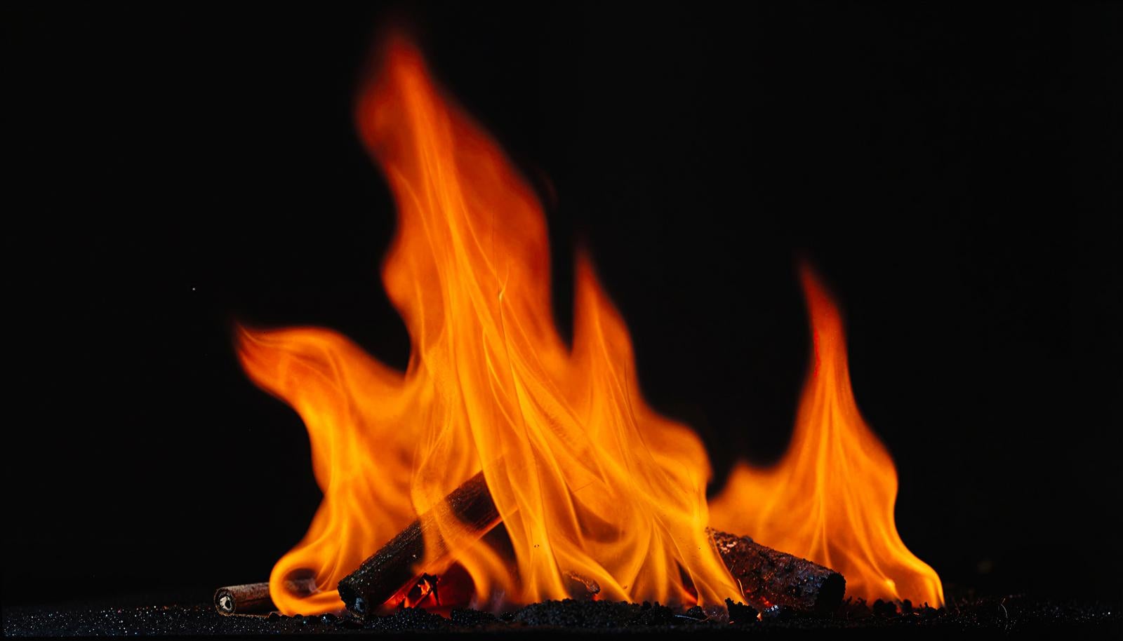 Vibrant flames transitioning from yellow to orange and red rise intensely above black firewood