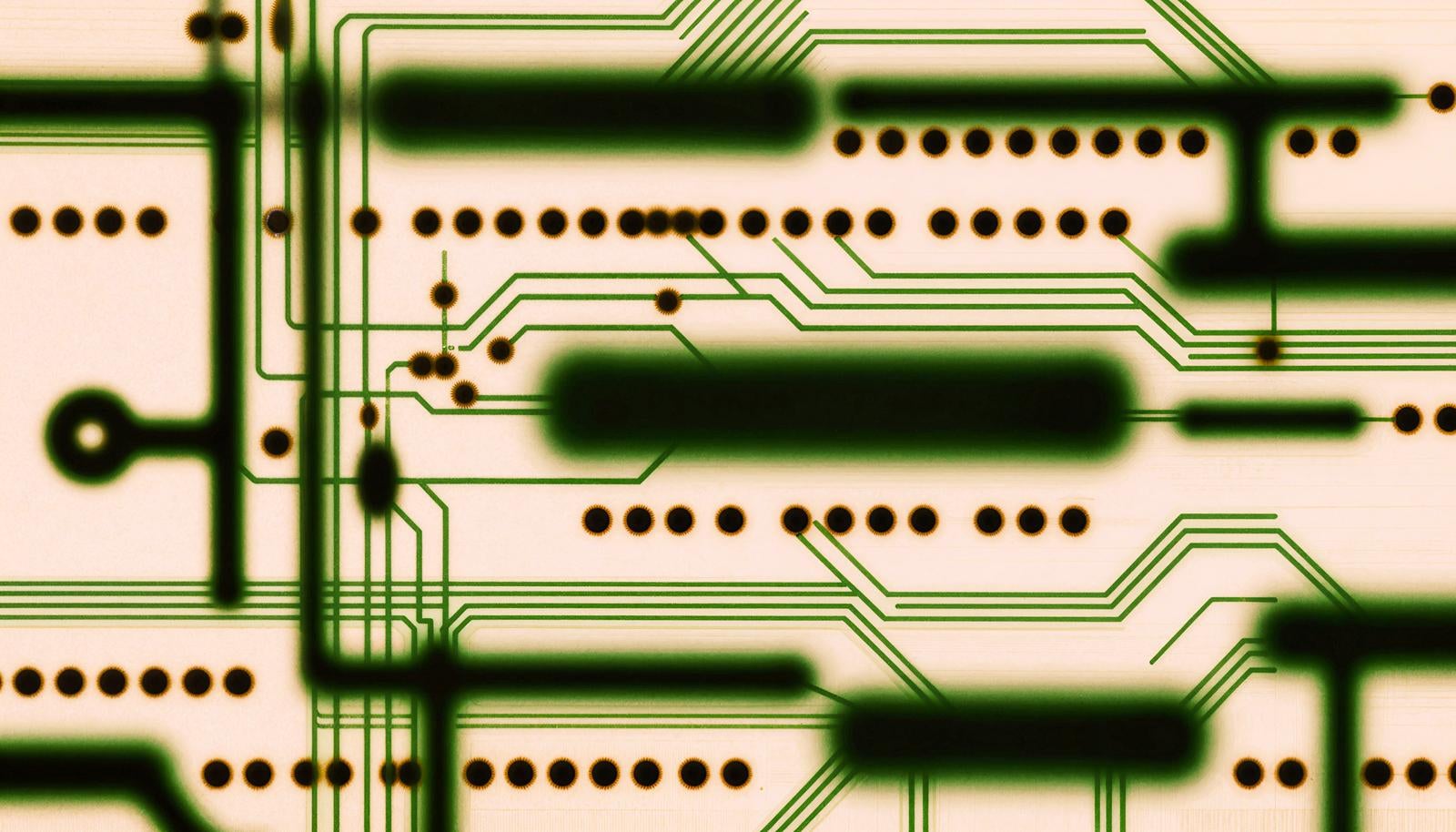 Close-up of electronic circuit board with green wiring patterns and through holes arranged in rows
