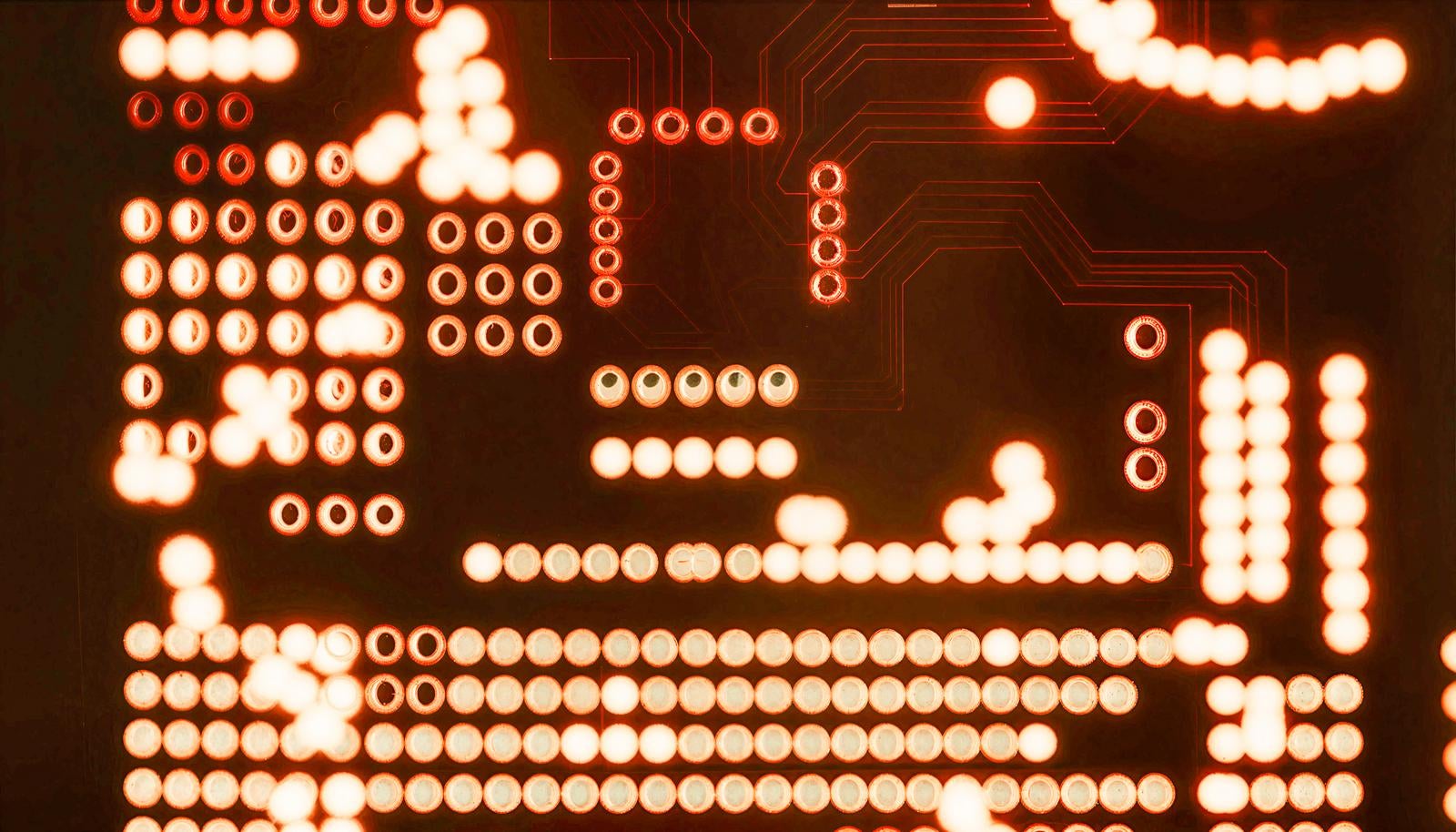 バックライトで透過したオレンジ色に光る電子回路基板のスルーホールと配線パターンのマクロ画像