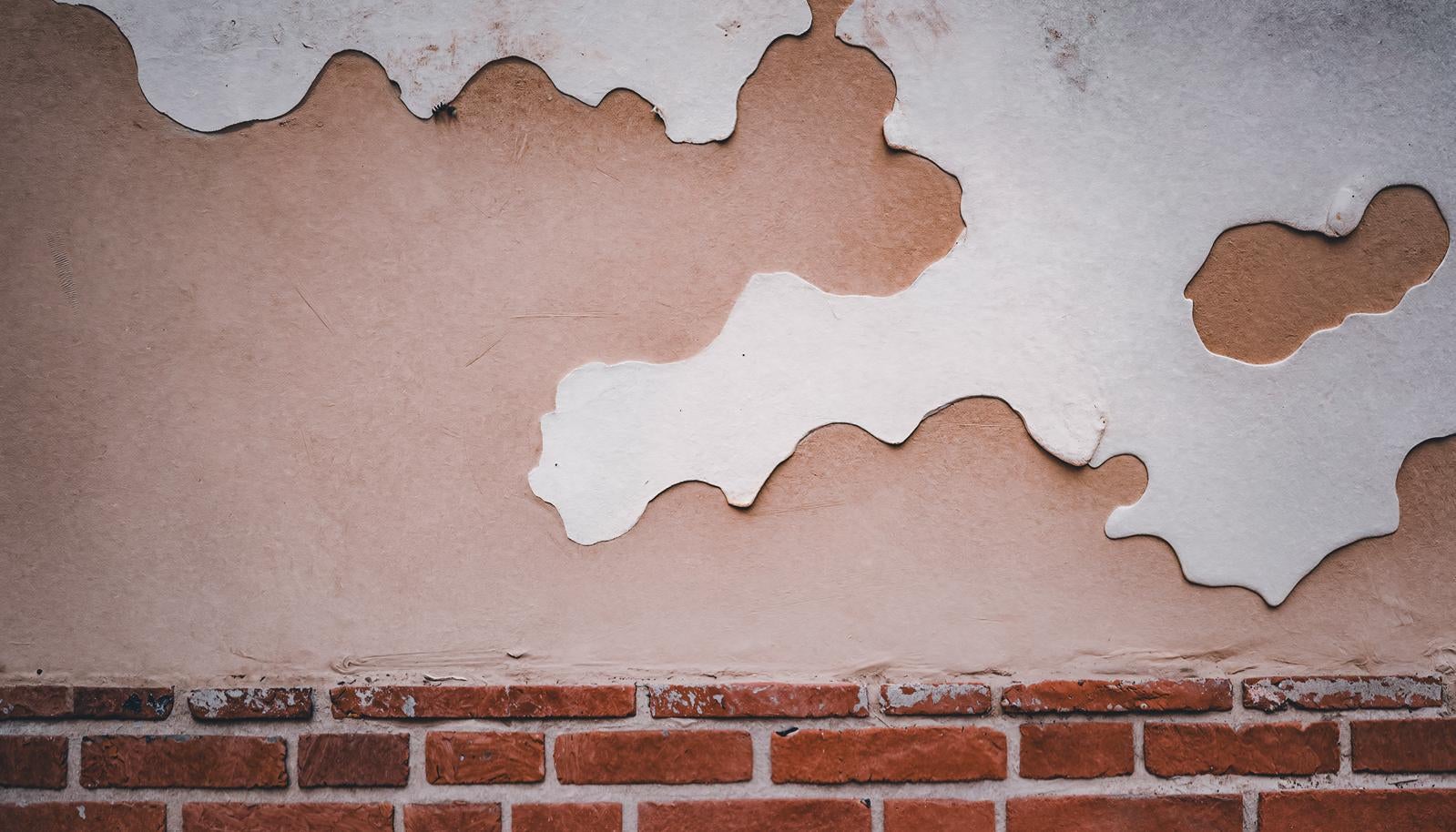 Close-up of a fence with large areas of plaster (Shikkui) peeling away, revealing the underlying earthen wall and brick base.