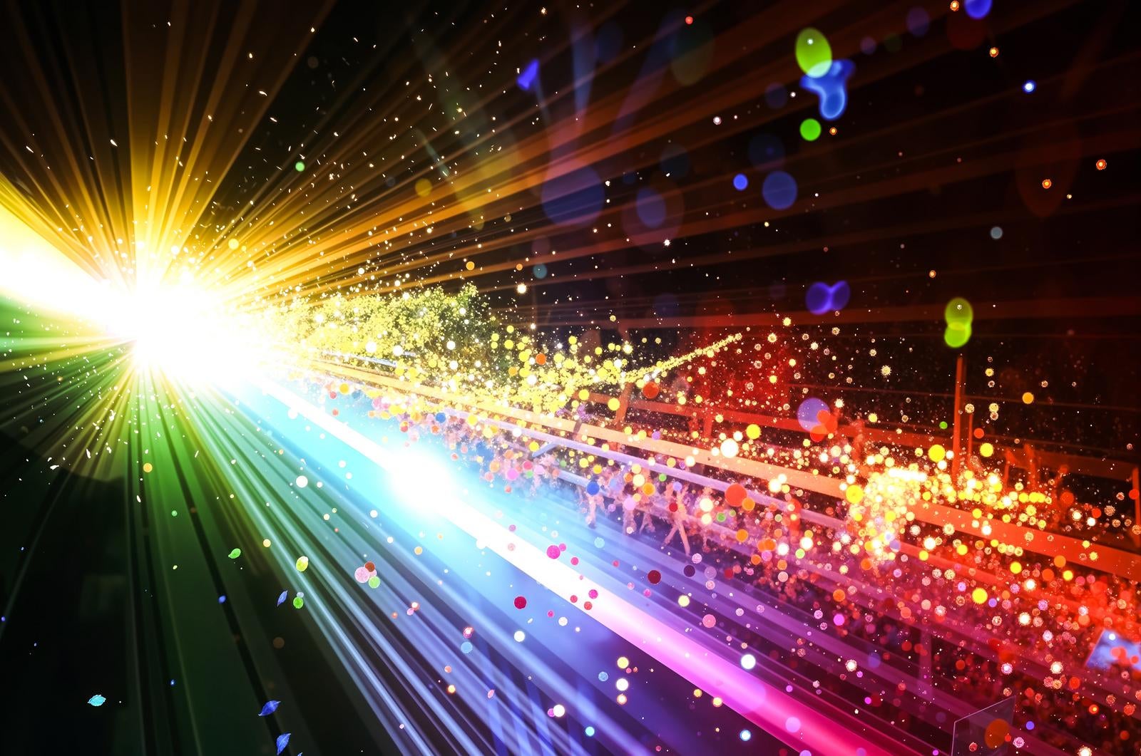 A CG image with rainbow-colored light rays radiating from the left side in the darkness with countless particles scattering