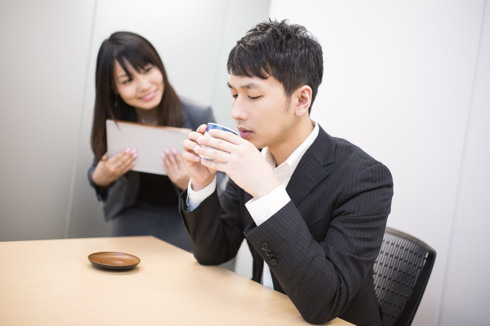 「女性社員に見つめられながらお茶をすするビジネスマン」の写真［モデル：大川竜弥 Lala］