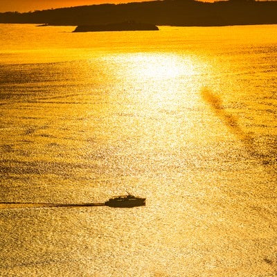 黄金色に輝く夕刻の海と渡し船の写真