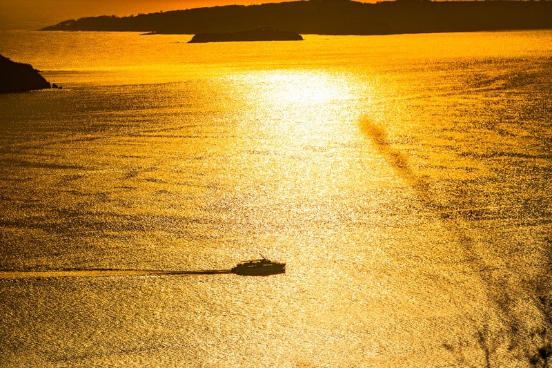黄金色に輝く夕刻の海と渡し船の写真
