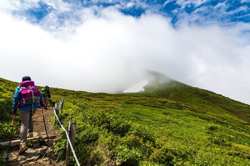 沸き立つ雲の中へと進む登山者（秋田駒ヶ岳）の写真