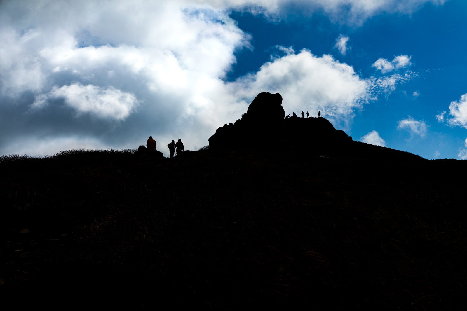「山頂に並ぶ登山者達のシルエットと沸き立つ雲（三ツ石山）」の写真