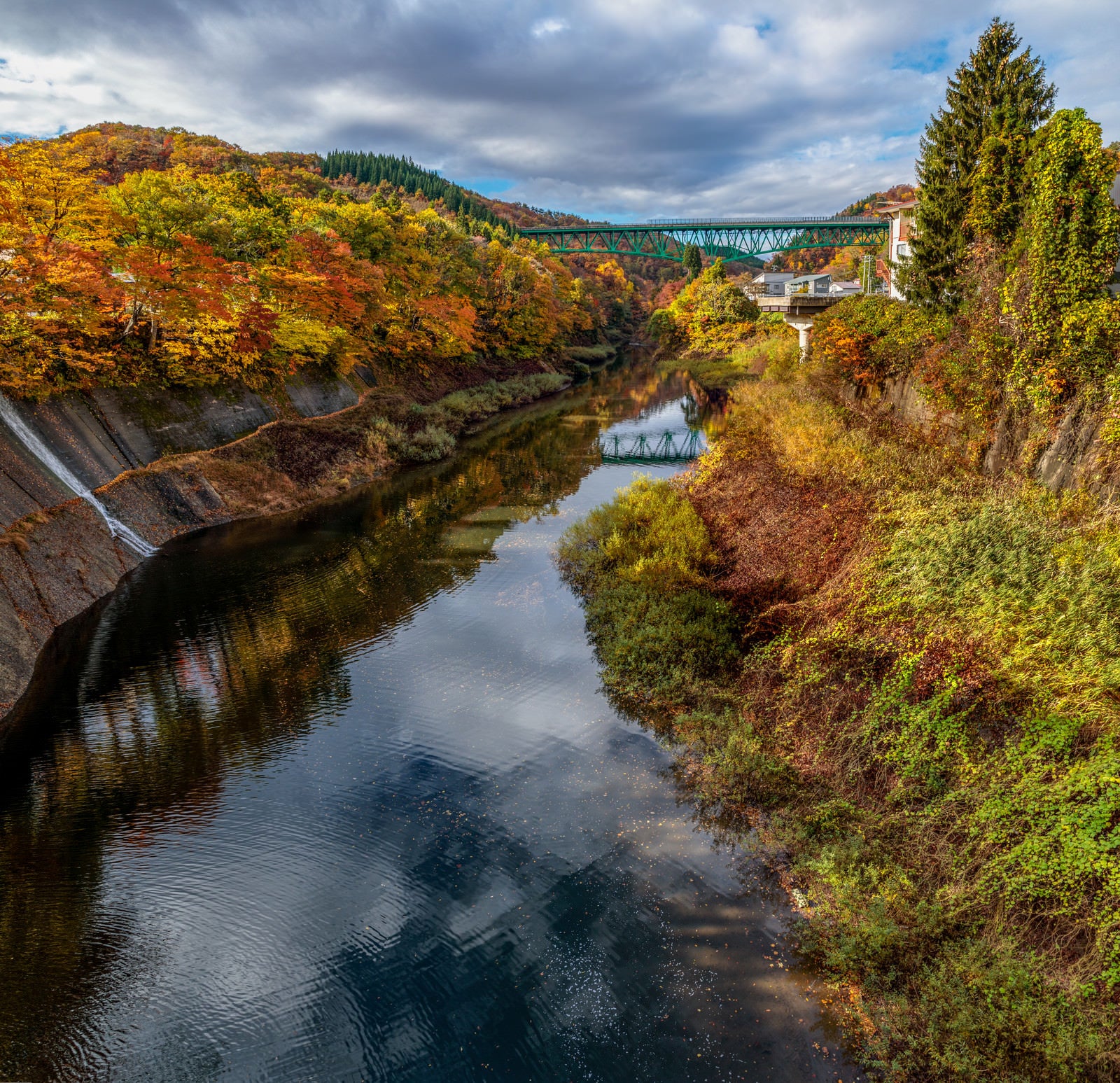 「鉄橋に向かう水路沿いの紅葉した木々とリフレクション」の写真