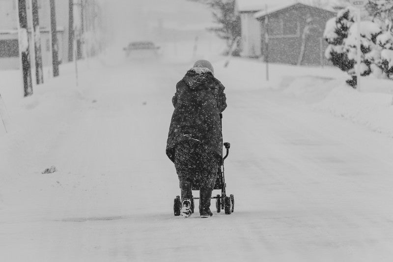 雪が降る中、移動する豪雪地帯に住む高齢者の写真