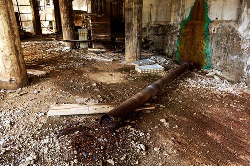 錆びて折れた配管と廃墟の写真