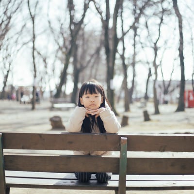 公園のベンチで退屈そうにする少女の写真