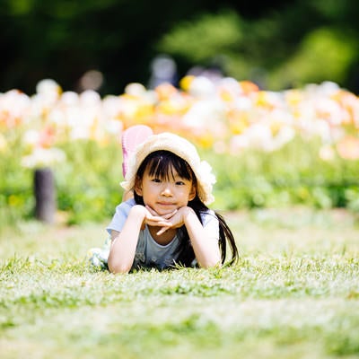 花畑の前で横になってくつろぐ麦わら帽子の女の子の写真