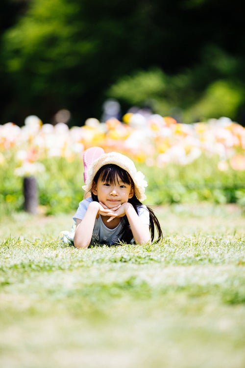 花畑の前で横になってくつろぐ麦わら帽子の女の子の写真