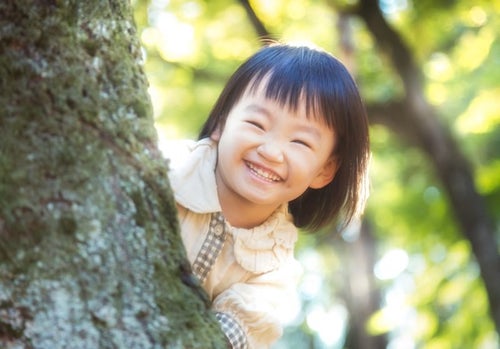木陰からニコニコ笑顔の小さい女の子の写真