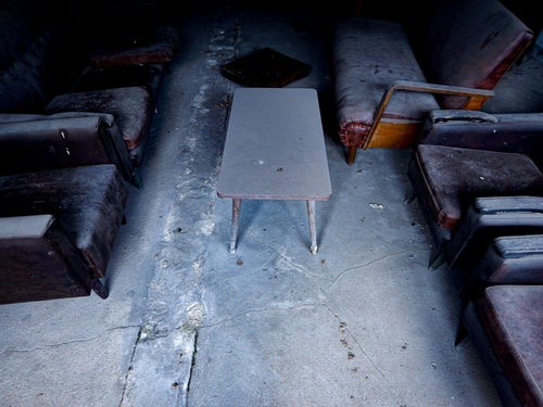 廃屋の埃まみれのテーブルとソファー（応接室跡）の写真