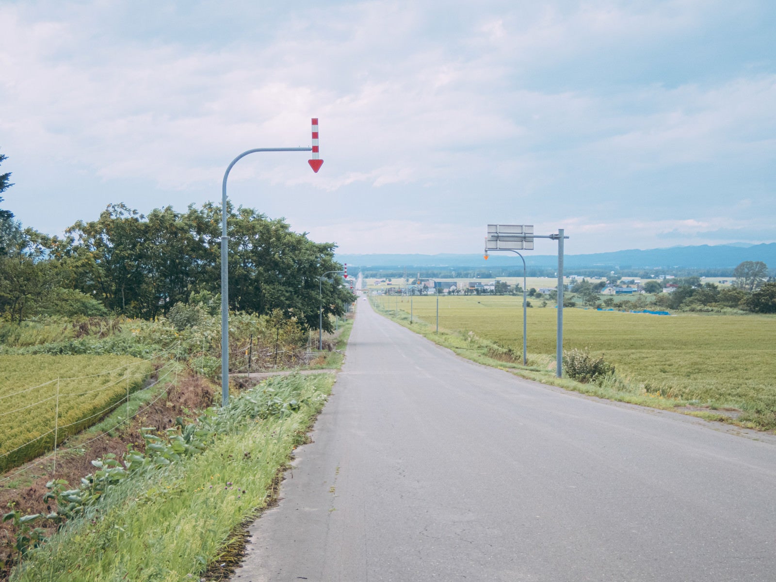 「北海道の長い一直線の道路と矢羽根付きポール」の写真