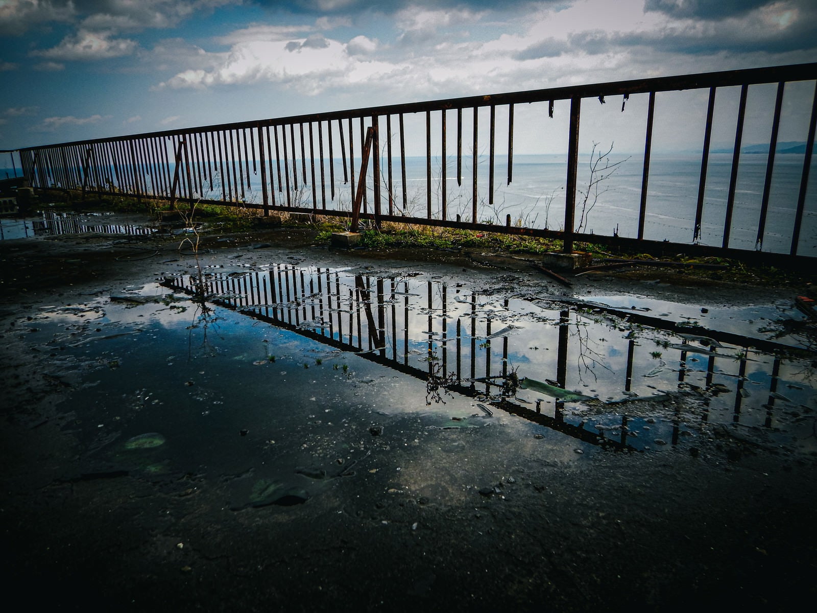 「水たまりに写り込んだ空と壊れた柵」の写真