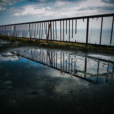 水たまりに写り込んだ空と壊れた柵の写真