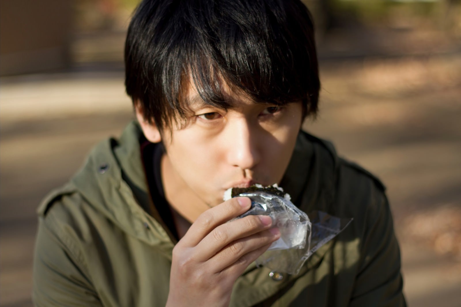 「外でコンビニおにぎりを食べる孤独な男性」の写真［モデル：大川竜弥］