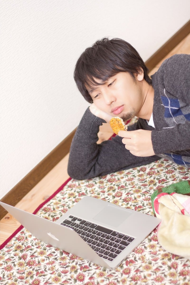 「横になり寝ながらノートパソコンを触る男性」の写真［モデル：大川竜弥］