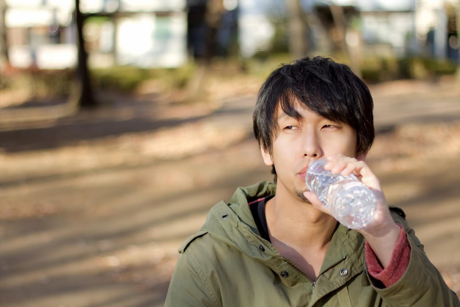 「寂しく公園でペッドボトルの水を飲む男性」の写真［モデル：大川竜弥］