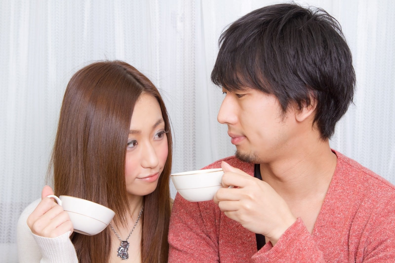 「コーヒーカップを持って見つめ合う恋人」の写真［モデル：大川竜弥 北野佑々］
