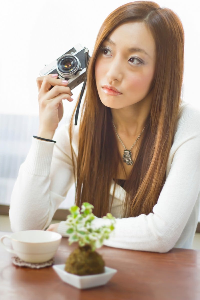 「レトロなカメラを持って肘をつく女性」の写真［モデル：北野佑々］