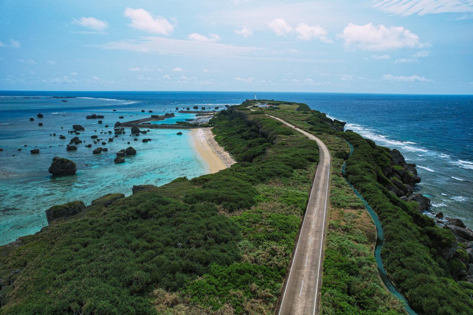 「平安名埼灯台まで続く道と美しい岩礁の海（空撮）」の写真