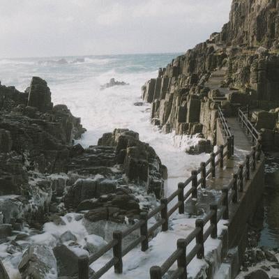 荒れた海が咲かせる波の花が寄せる岩場や歩道の写真