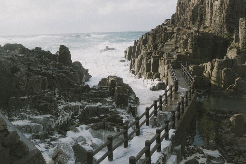 荒れた海が咲かせる波の花が寄せる岩場や歩道の写真