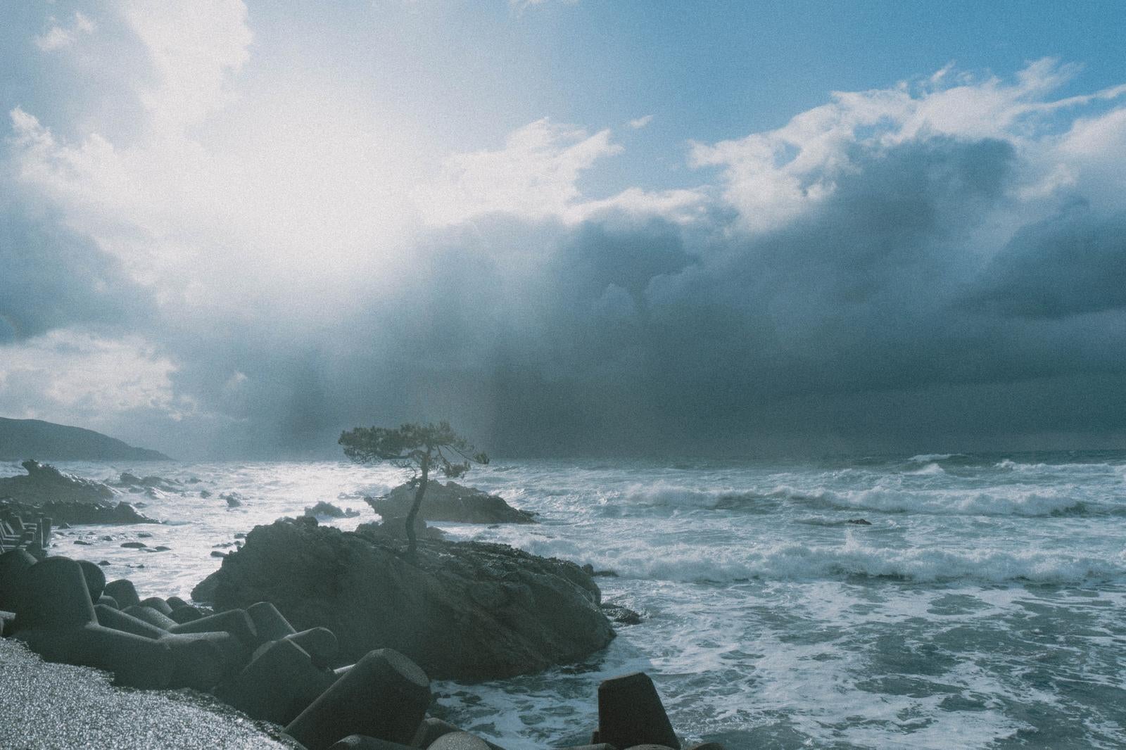 「黒雲と青空が対比する荒波の海岸線」の写真