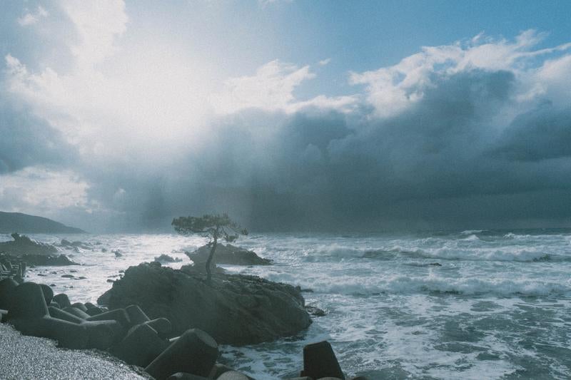 黒雲と青空が対比する荒波の海岸線の写真