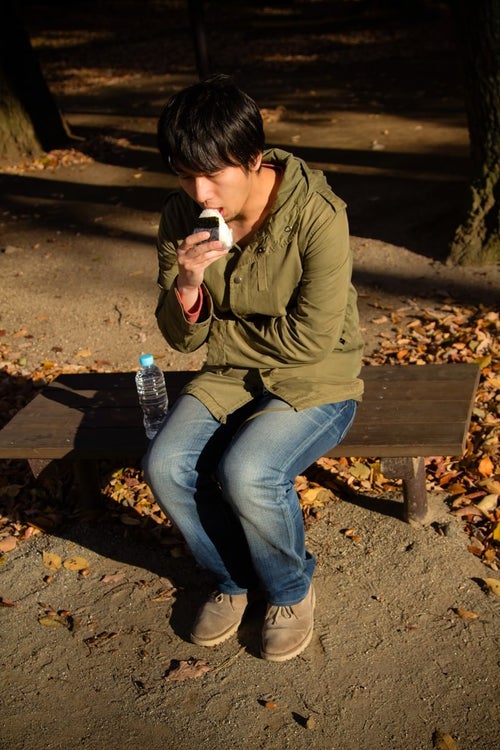 公園で寂しくおにぎりを食べる男性の写真