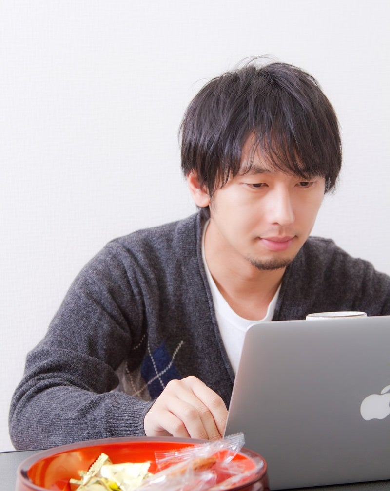 「お菓子食べながらパソコンをする男性」の写真［モデル：大川竜弥］