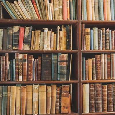 古い洋書が並ぶ木製の本棚、歴史を感じさせるアンティークな書籍コレクションの写真