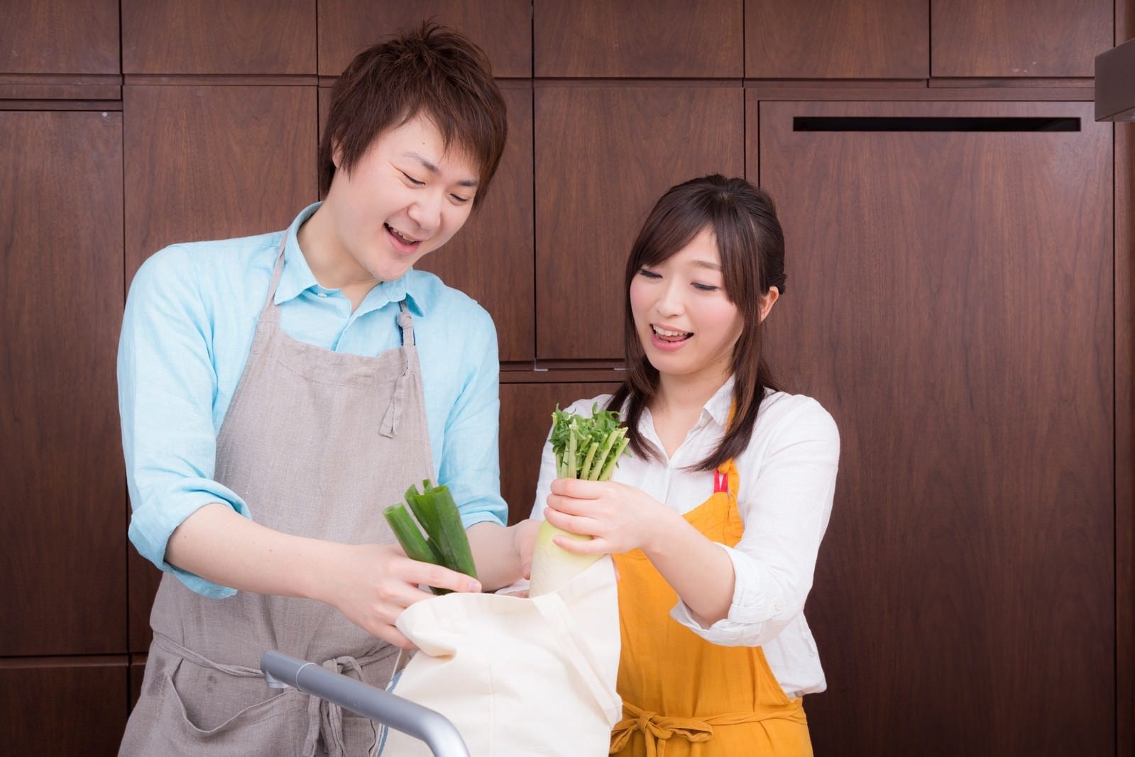 「買い物袋から野菜を取り出して料理を始める二人」の写真［モデル：五十嵐夫妻］