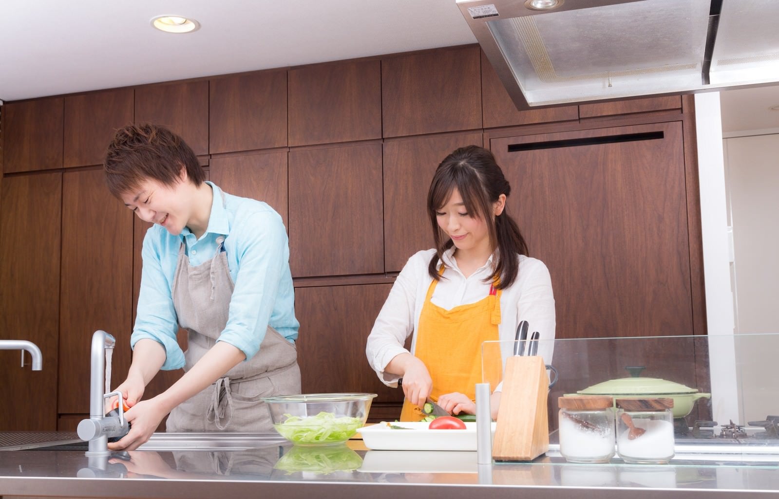 「仲睦まじくキッチンで料理をする若い夫婦」の写真［モデル：五十嵐夫妻］