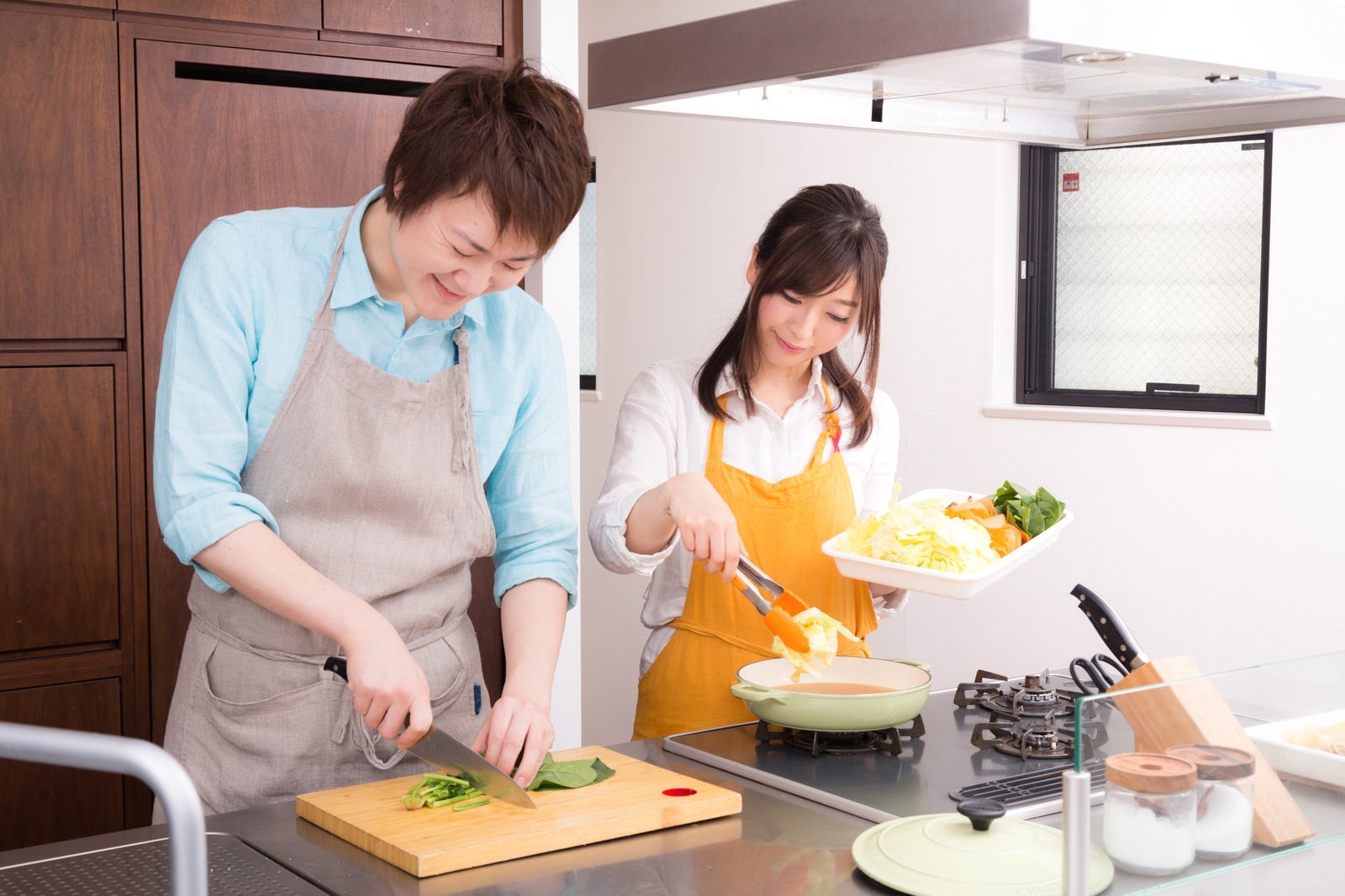 「キッチンでお鍋を一緒に作っている夫婦」の写真［モデル：五十嵐夫妻］