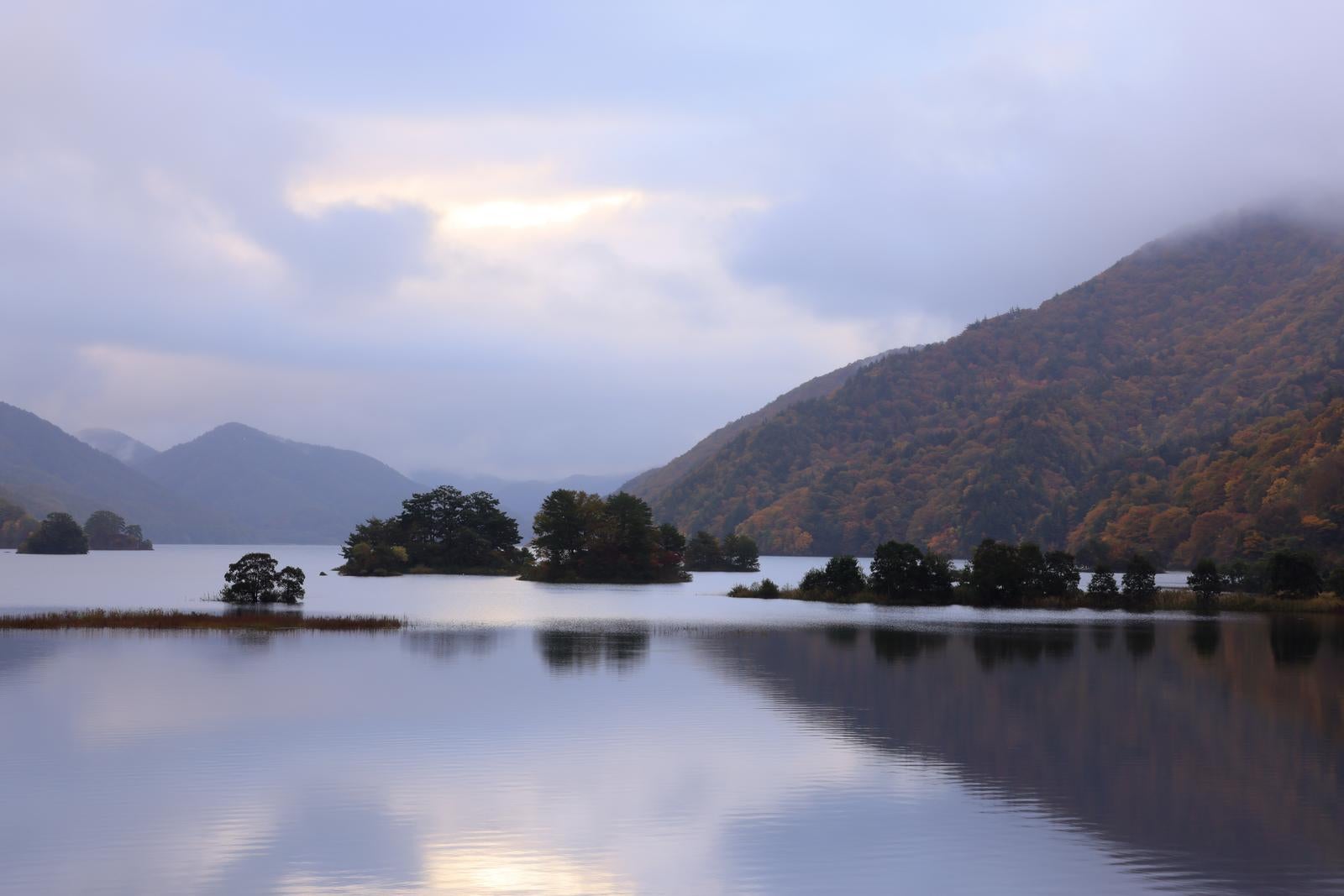 「湖面に映る静寂な美しさと雲間の朝焼けが照らす秋元湖」の写真