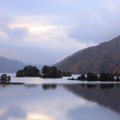 湖面に映る静寂な美しさと雲間の朝焼けが照らす秋元湖の写真