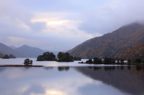 湖面に映る静寂な美しさと雲間の朝焼けが照らす秋元湖の写真